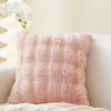 A fluffy pink faux fur decorative pillow resting on a white surface next to a light-colored wall.