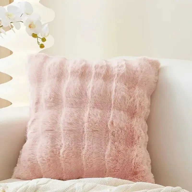 A fluffy pink faux fur decorative pillow resting on a white surface next to a light-colored wall.