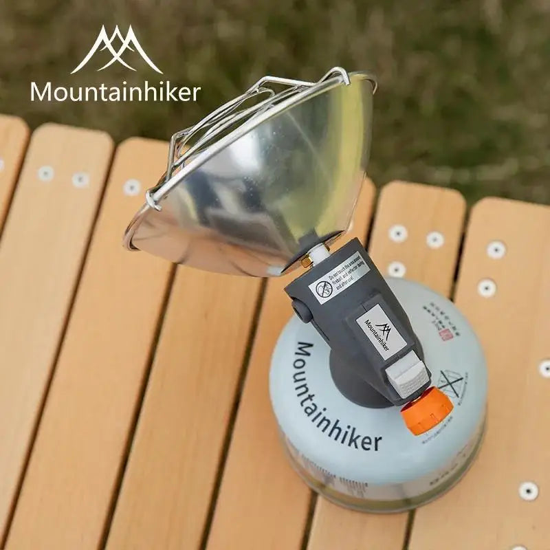 A silver portable butane gas stove with a flared cup is shown resting on a wooden surface.