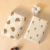 A beige soft cotton gauze baby swaddle blanket with brown bear patterns and a fluffy white pom-pom.