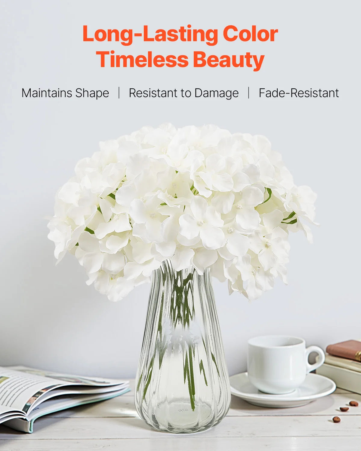 A bouquet of white silk hydrangea flowers displayed in a clear glass vase on a white surface.