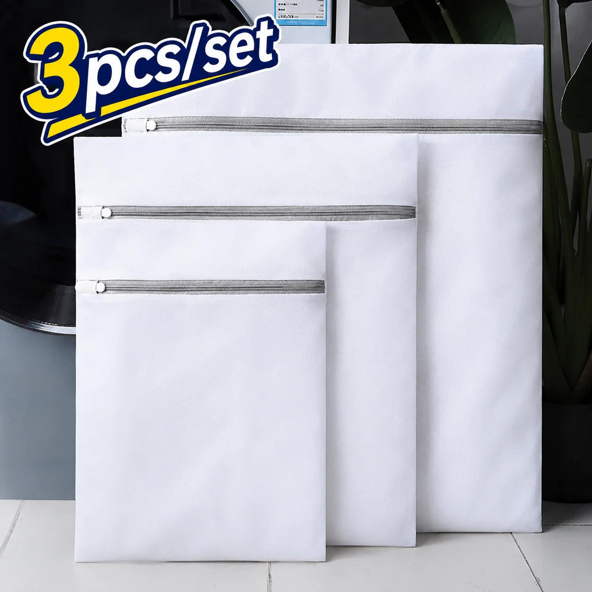 A set of three white mesh laundry bags with silver zippers are displayed on a white surface.