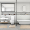 A modern bathroom featuring a white toilet, a large bathtub, and several beige bath mats on the floor.