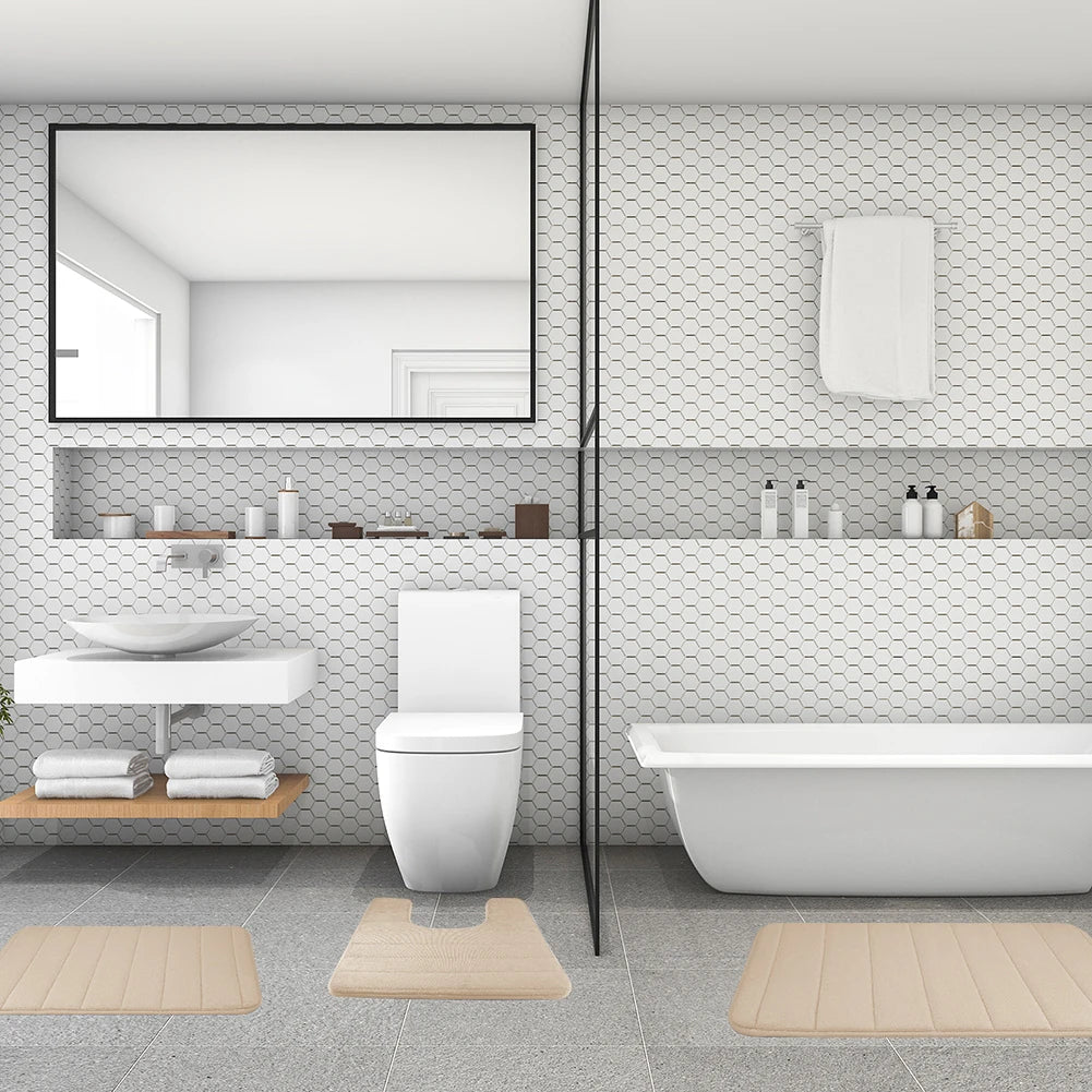 A modern bathroom featuring a white toilet, a large bathtub, and several beige bath mats on the floor.