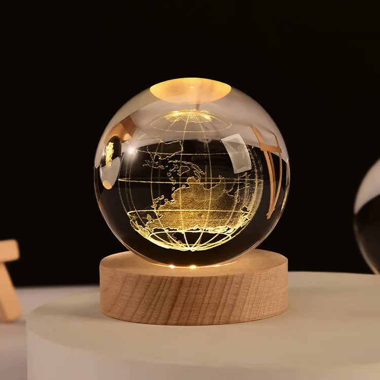 A spherical crystal ball night light with a golden internal glow resting on a natural wooden base.