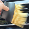 A hand is holding a black detailing brush set with soft yellow bristles inside a car interior cleaning device.