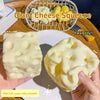 Eine Hand hält einen großen, quetschbaren, gelben Käse-förmigen Stressball neben einen Drahtkorb mit Käse und gelben Artikeln