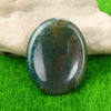 A smooth, oval green and brown natural crystal stone resting on bright green grass.