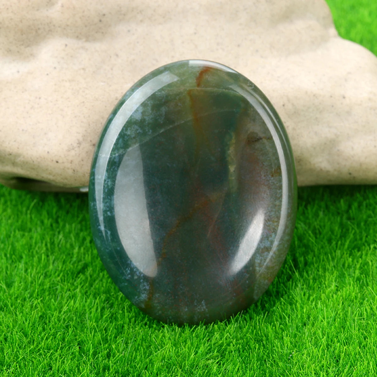 A smooth, oval green and brown natural crystal stone resting on bright green grass.