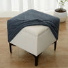 A navy blue geometric jacquard stretch ottoman cover draped over a white upholstered ottoman.