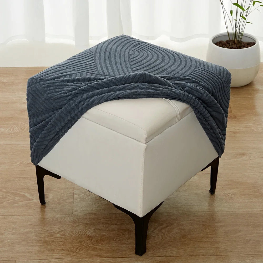 A navy blue geometric jacquard stretch ottoman cover draped over a white upholstered ottoman.
