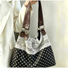 Sac à l'épaule noir et blanc à pois, avec un overlay en dentelle blanche et des sangles en cuir marron.