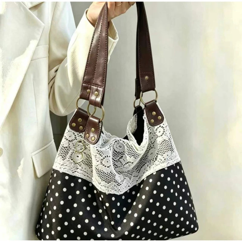 Sac à l'épaule noir et blanc à pois, avec un overlay en dentelle blanche et des sangles en cuir marron.