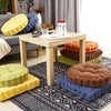 A collection of thick corduroy floor cushions in yellow, blue, green, and brown are arranged on a rug.