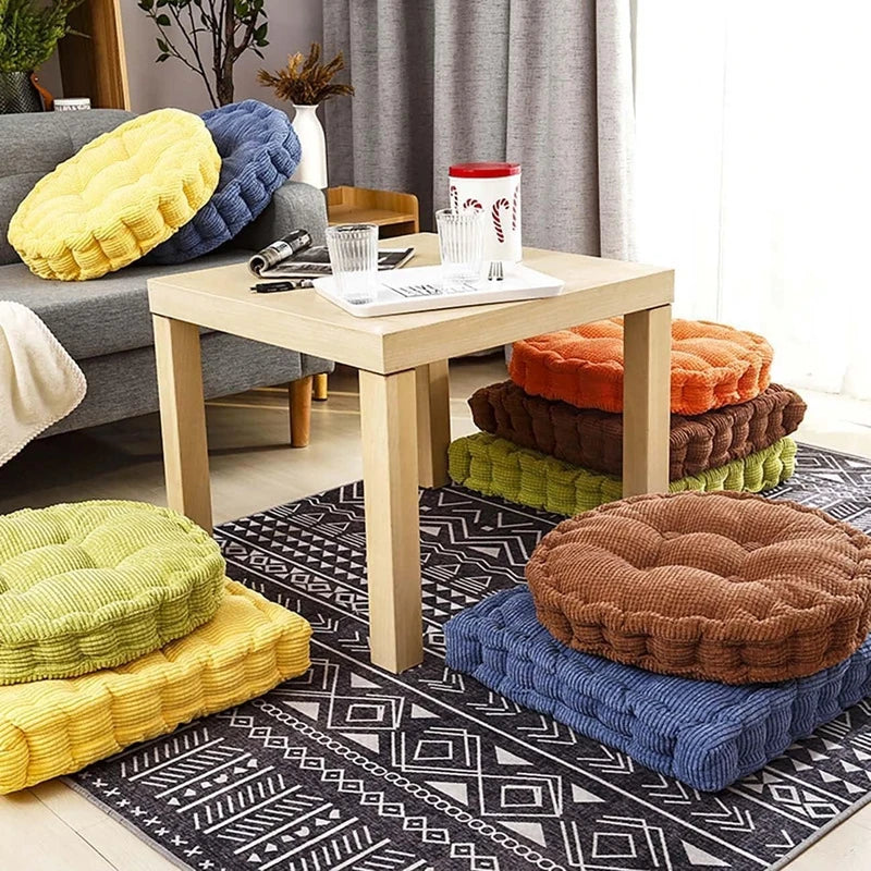 A collection of thick corduroy floor cushions in yellow, blue, green, and brown are arranged on a rug.