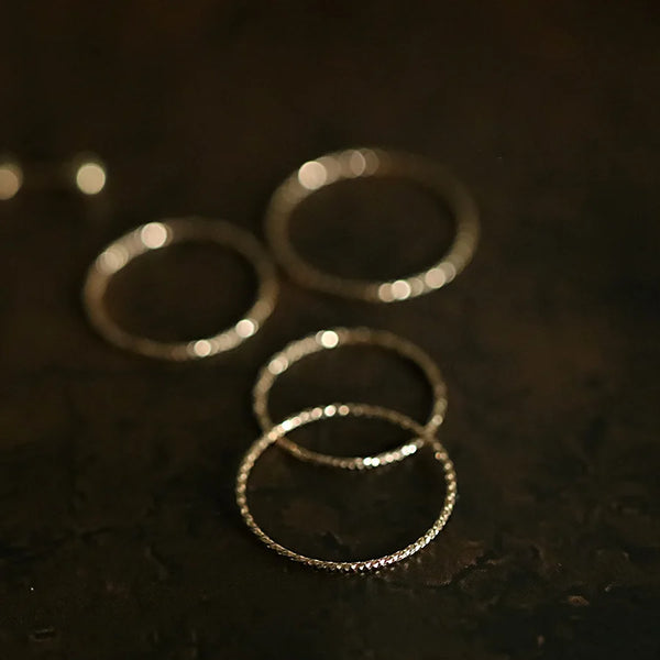 Primer plano de varios anillos minimalistas de plata chapada en reposo sobre una superficie oscura.