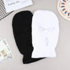 A pair of knitted black and white ski mask car headrest covers lying on a light gray surface.
