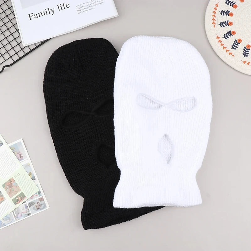 A pair of knitted black and white ski mask car headrest covers lying on a light gray surface.