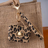 A leopard print PU leather mini wallet attached to a gold keychain, resting on a beige canvas bag.