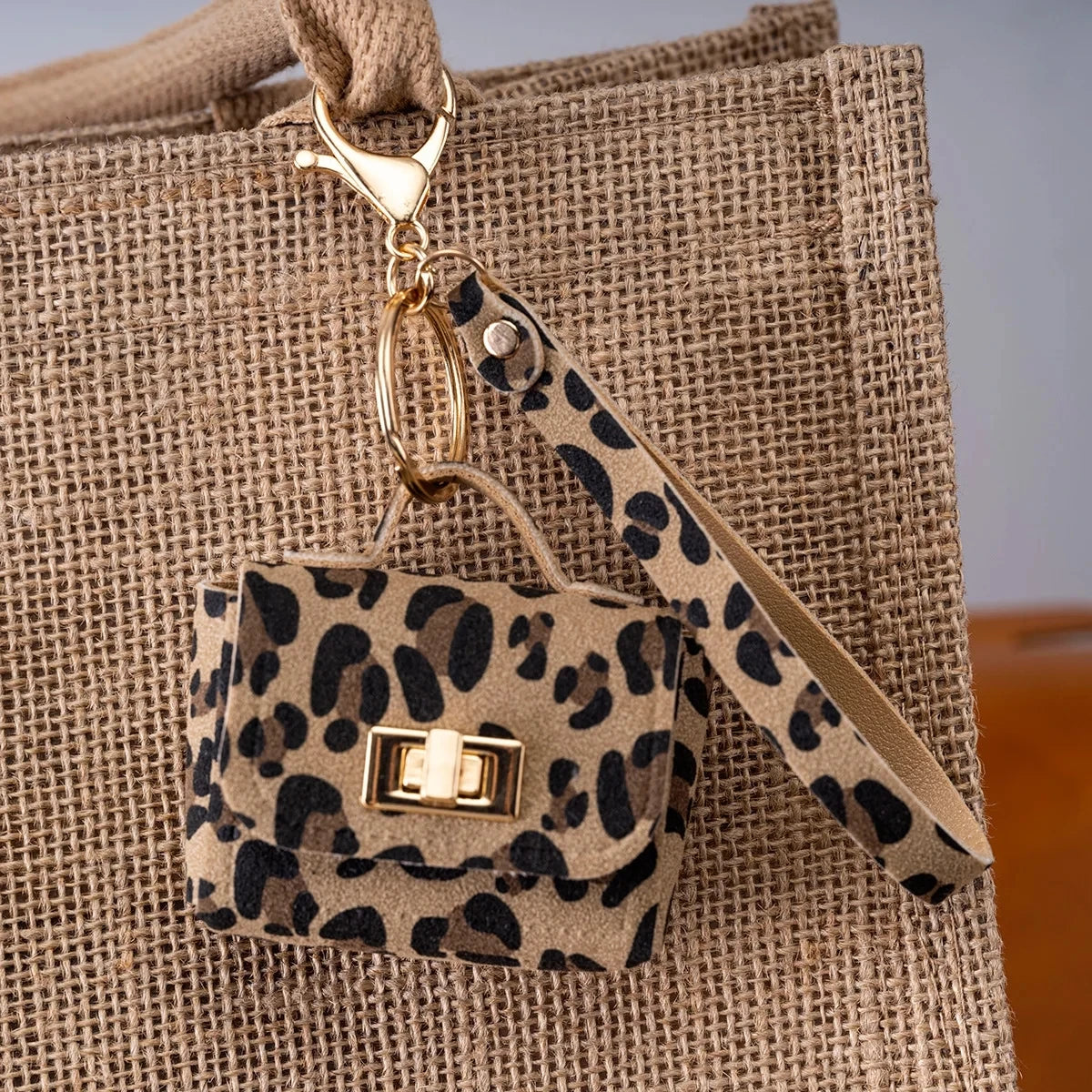 A leopard print PU leather mini wallet attached to a gold keychain, resting on a beige canvas bag.