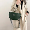 A woman holds a dark green woven pattern waist bag with gold chain strap against a light beige trench coat.