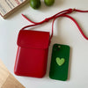 A red vintage PU leather crossbody bag is shown next to a green smartphone and a red strap on a white surface.