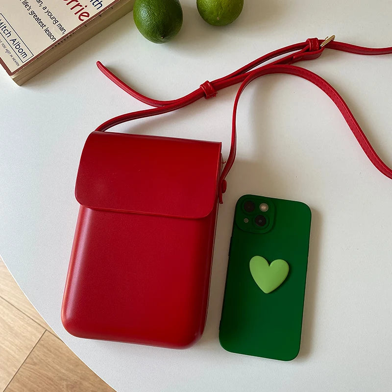 A red vintage PU leather crossbody bag is shown next to a green smartphone and a red strap on a white surface.