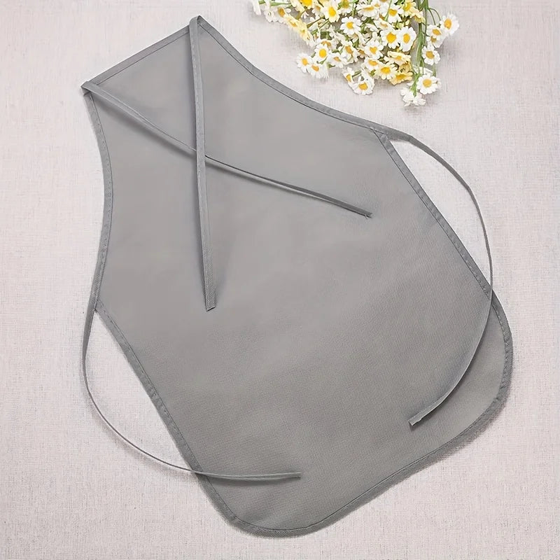 A light gray non-woven fabric craft apron is displayed on a white cloth next to a small bouquet of white and yellow flowers.