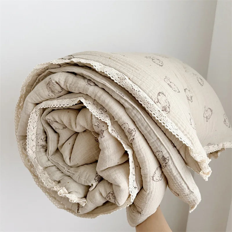 A rolled floral muslin baby blanket in beige with embroidered designs