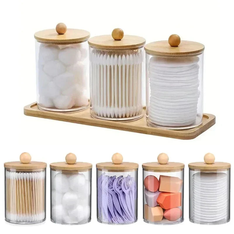 A set of clear acrylic apothecary jars with wooden lids filled with white and purple bath salts or decorative stones.