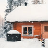 A wooden house with a snow-covered roof and a barbecue grill cover in the foreground.