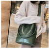 A woman wearing a beige sweater holds a dark green alligator pattern crossbody bag.
