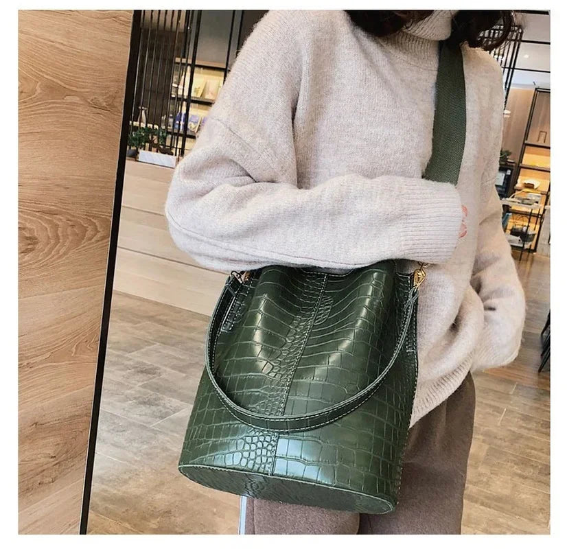 A woman wearing a beige sweater holds a dark green alligator pattern crossbody bag.