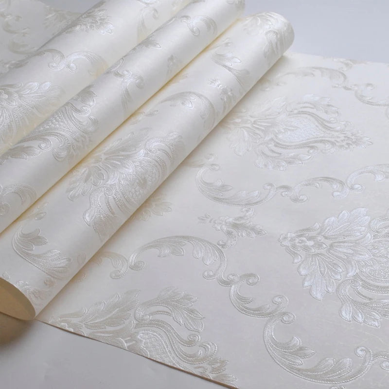 Rolls of embossed damask wallpaper featuring a delicate floral design on a white background.