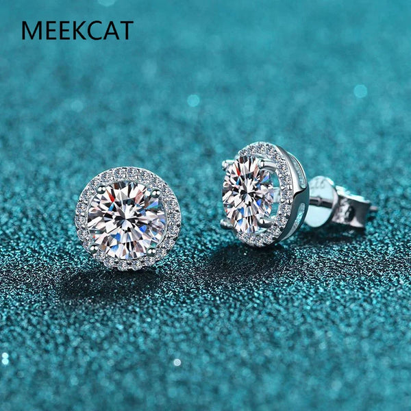 Ein Paar funkelnder Moissanit-Steckstecker, präsentiert auf einer dunklen, glitzernden blaugrünen Oberfläche.