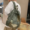 A person is holding a olive green canvas patchwork backpack in a light indoor setting.