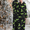 A woman models an oversized black hoodie blanket featuring a green dinosaur print in a bright indoor setting.