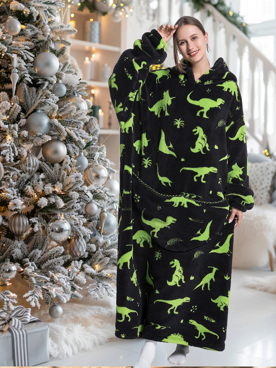 A woman models an oversized black hoodie blanket featuring a green dinosaur print in a bright indoor setting.