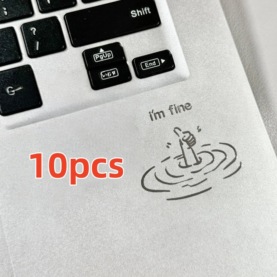 A close-up of a white laptop keyboard showing various stickers and a hand gesture drawing 'I'm fine'.