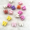 A collection of 10 mixed alphabet letter beads in various pastel colors like pink purple orange and white scattered on a whit