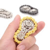 A hand holds a gold-toned sprocket fidget spinner, a metal desk toy for stress relief.