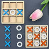 A set of wooden tic tac toe game pieces including blue and orange Xs and circles, with a pink tulip in the background.