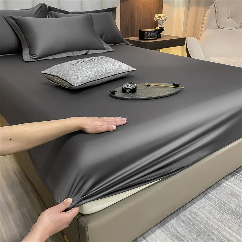 Un juego de sábanas ajustadas de algodón de lujo gris oscuro está tendido sobre una cama, con manos ajustando la tela.