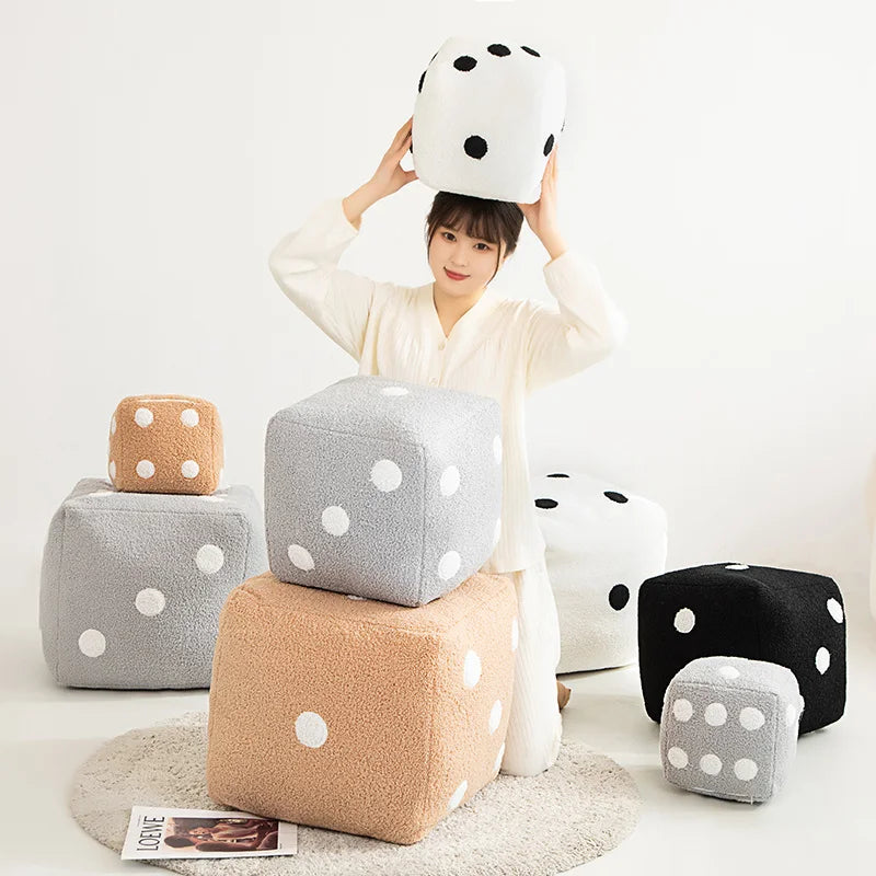 A person holds up a white and black polka-dotted plush pillow, with several similar gray and beige square pillows displayed a