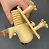 A hand holds a yellow playful animal toilet paper holder with outstretched limbs and a round body.