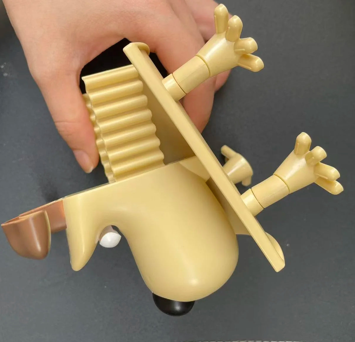 A hand holds a yellow playful animal toilet paper holder with outstretched limbs and a round body.