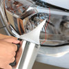 A hand is applying a white substance to the lens of a car headlight using a specialized tool.