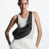 Model in white tank top and light trousers, holding a black leather crossbody bag.