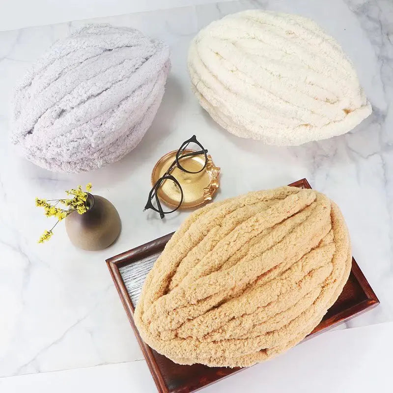 Three balls of extra thick chenille yarn in white and beige tones displayed on a marble surface.