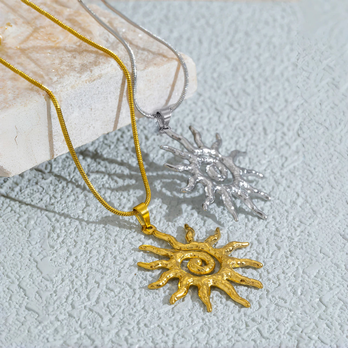 Goldspirale Sonnenanhänger-Kette auf hellem Stein vor grauem Hintergrund.